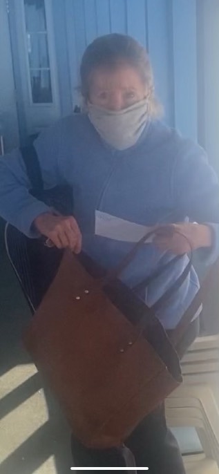 Maura Walsh sitting at her tennis club in Chappaqua, New York, wearing a face mask and blue sweatshirt, a brown leather bag beside her, being served legal documents by a process server