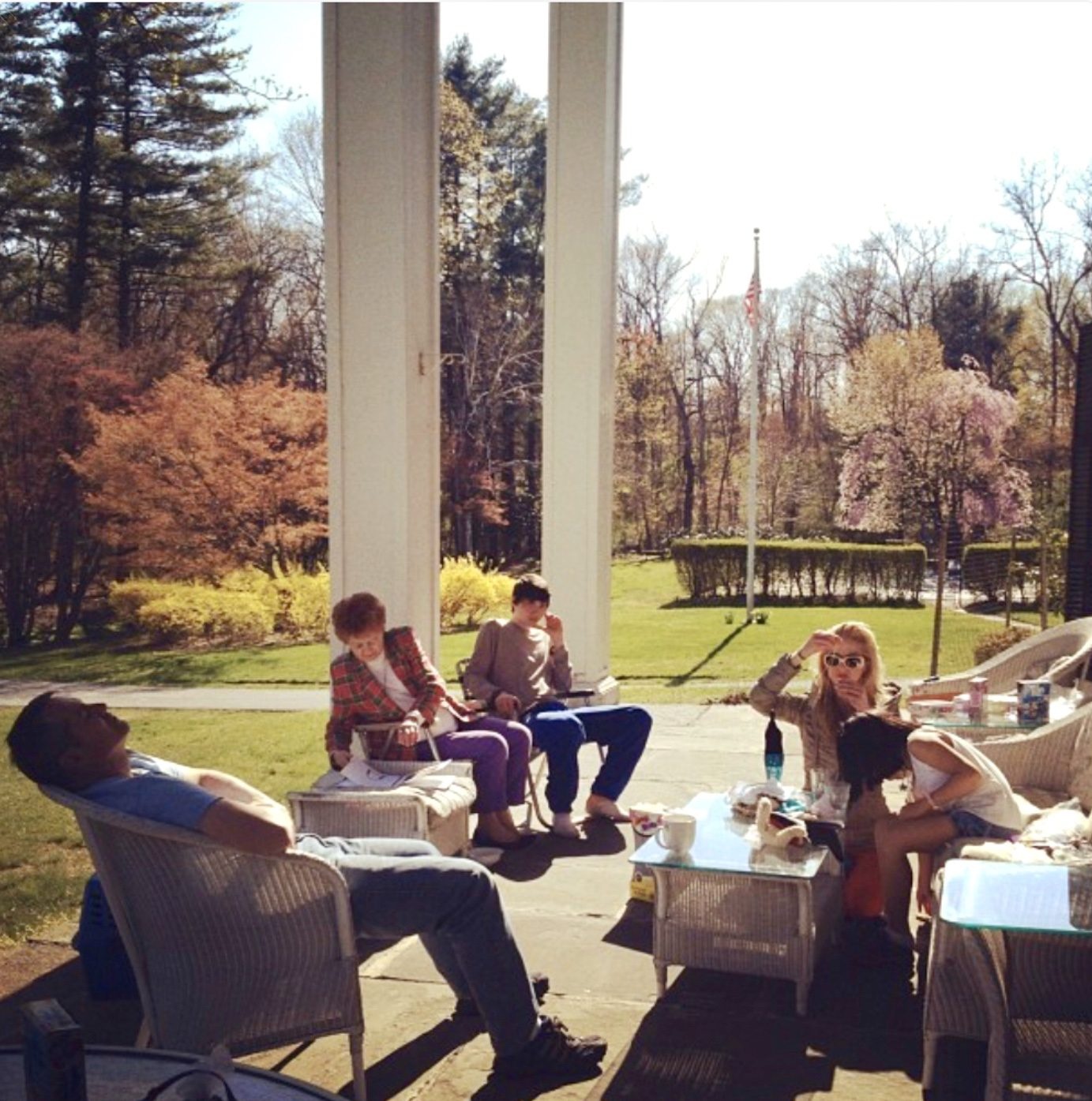 Walsh family on the columned porch at Tara Knoll, Chappaqua — cherry blossoms in full bloom, wicker furniture, glass coffee table, American flag visible through the columns